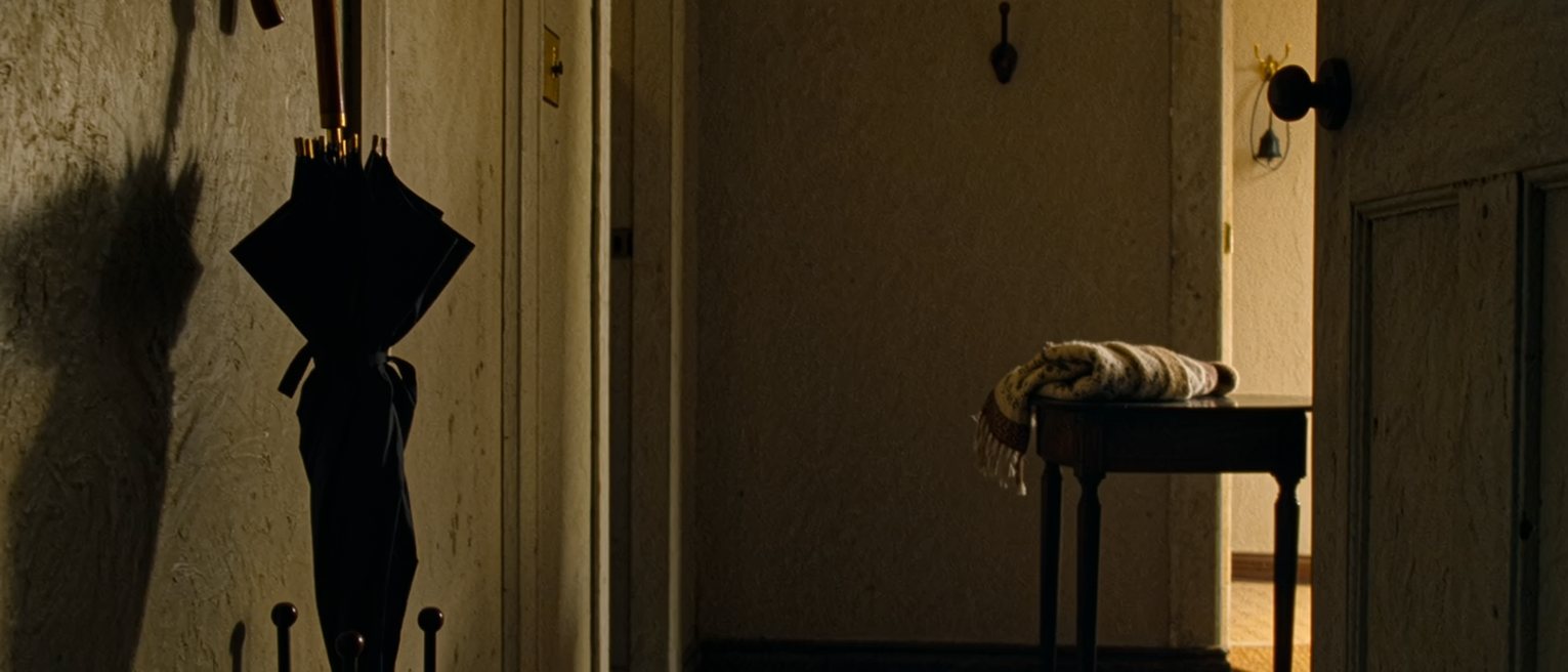 a hall with one umbrella in the stand and the second hook empty, a scarf folded and left on the table by the door