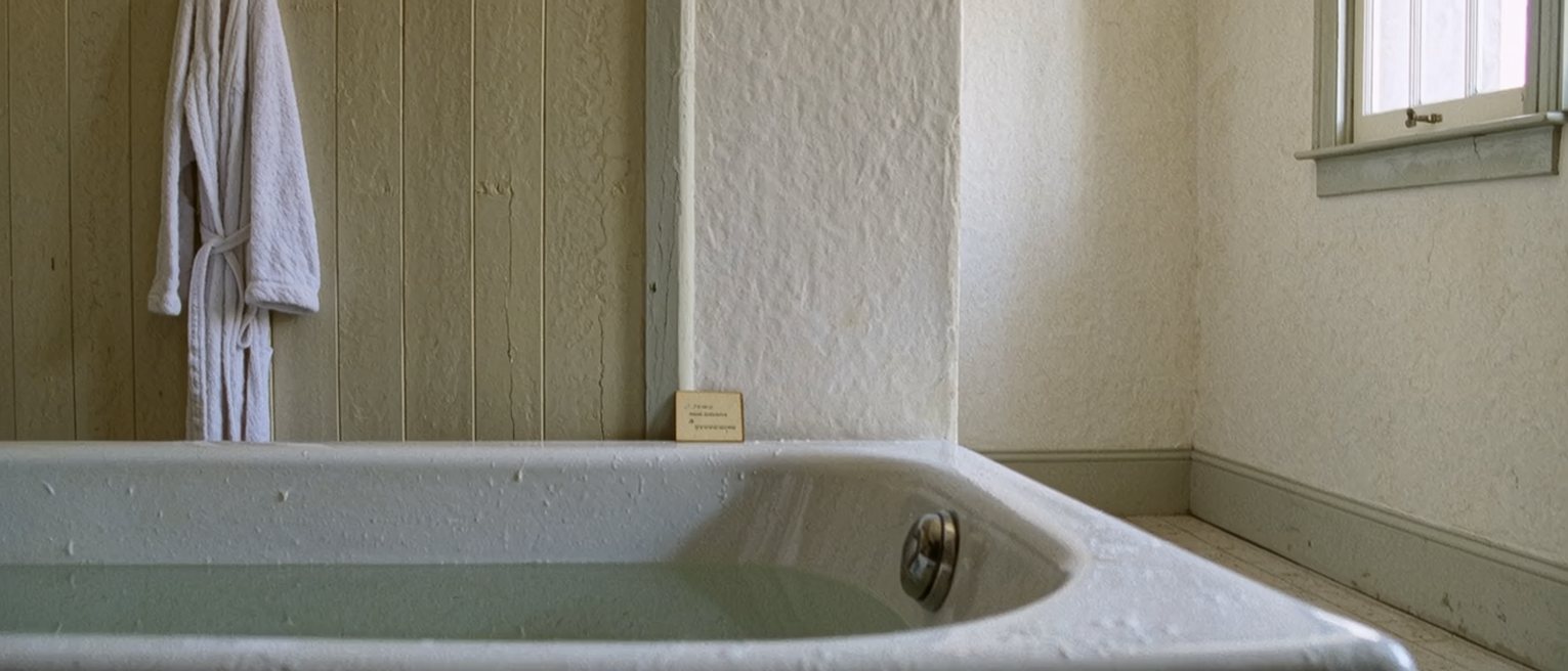 a bathroom with a bath run and a robe on the hook, and beside the bath a small card left face down