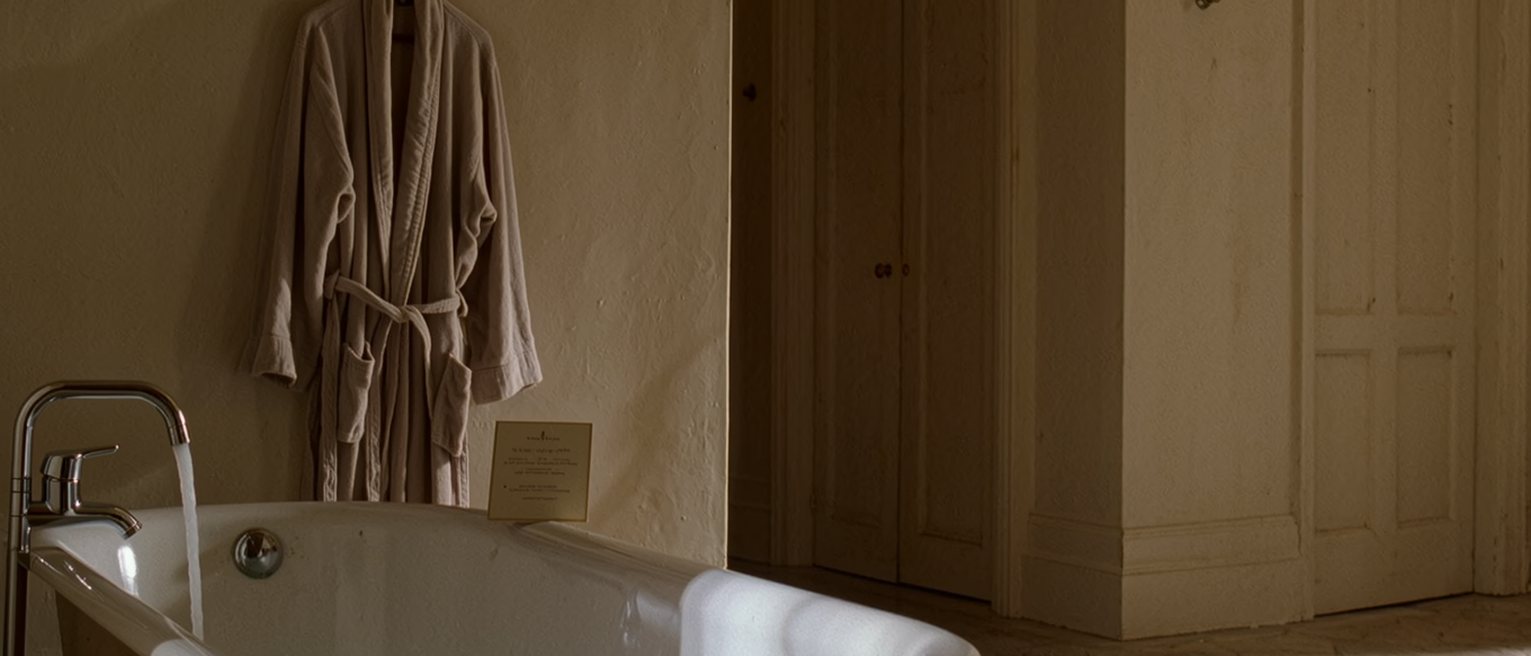 a bathroom with a bath run and a robe on the hook, and beside the bath a small card left face down