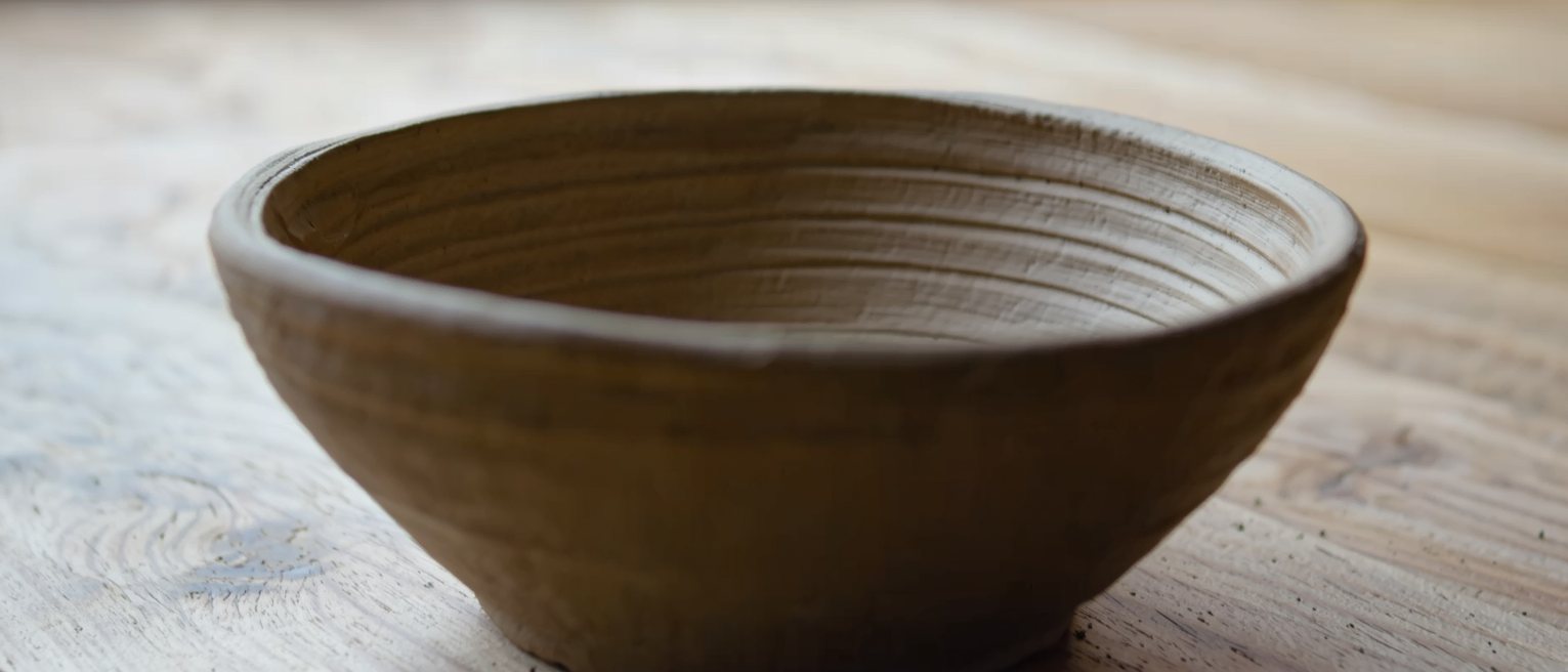 a hand-thrown clay bowl with the potter's finger ridges standing inside it