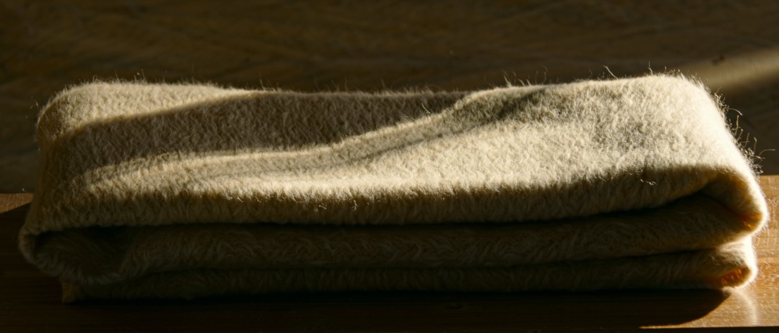 a wool blanket folded in four on a bench, the nap brushed one way