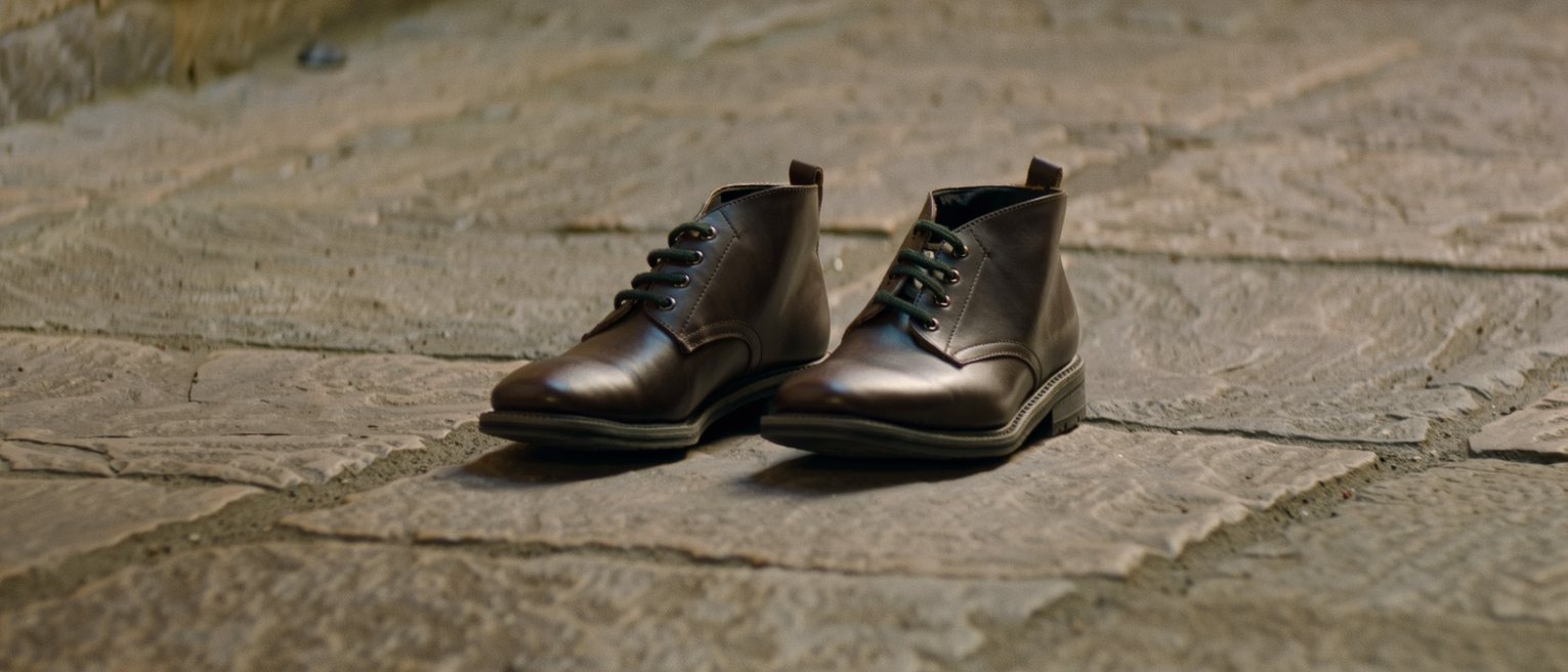 a pair of boots stood together and empty on a stone threshold, their laces still tied