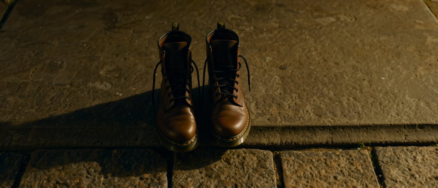 a pair of boots stood together and empty on a stone threshold, their laces still tied