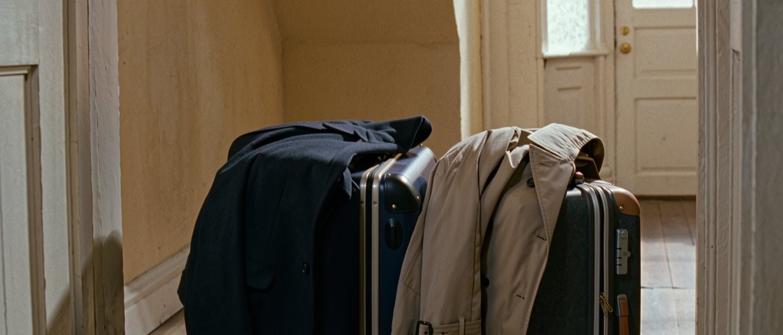 a hall with two packed suitcases standing by the front door and two coats laid over them, the flat behind tidied for leaving