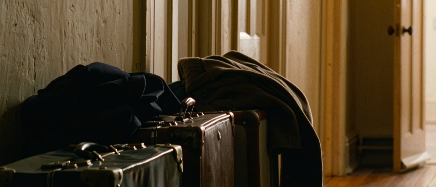 a hall with two packed suitcases standing by the front door and two coats laid over them, the flat behind tidied for leaving