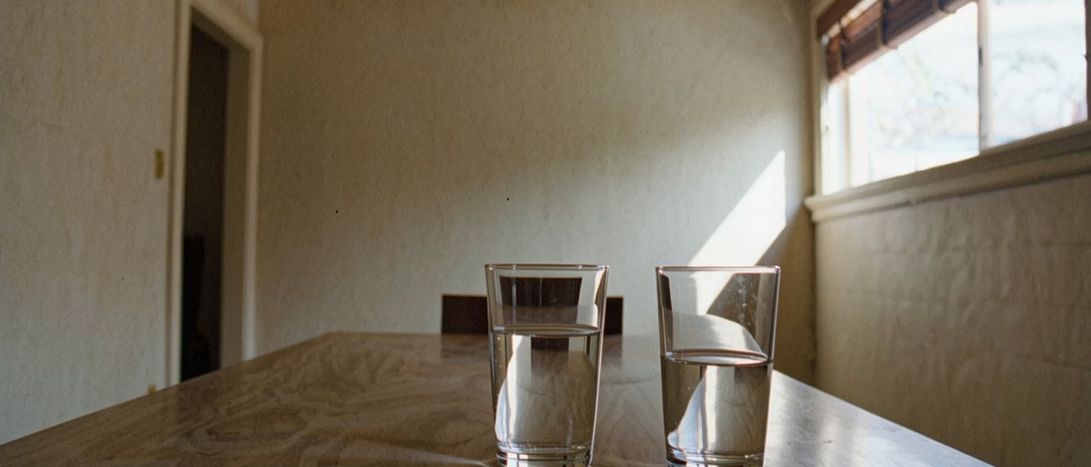 a dining table cleared except for two glasses, one full and one refilled, and a chair pulled round to the same side of the table as the other