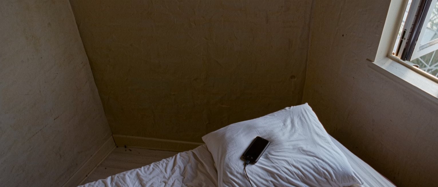 a bedroom with the covers turned back on one side only and a phone left charging on the far pillow