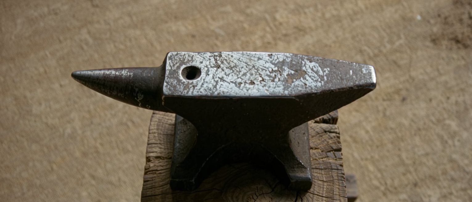 a heavy iron anvil on an oak block, its top worn bright from use