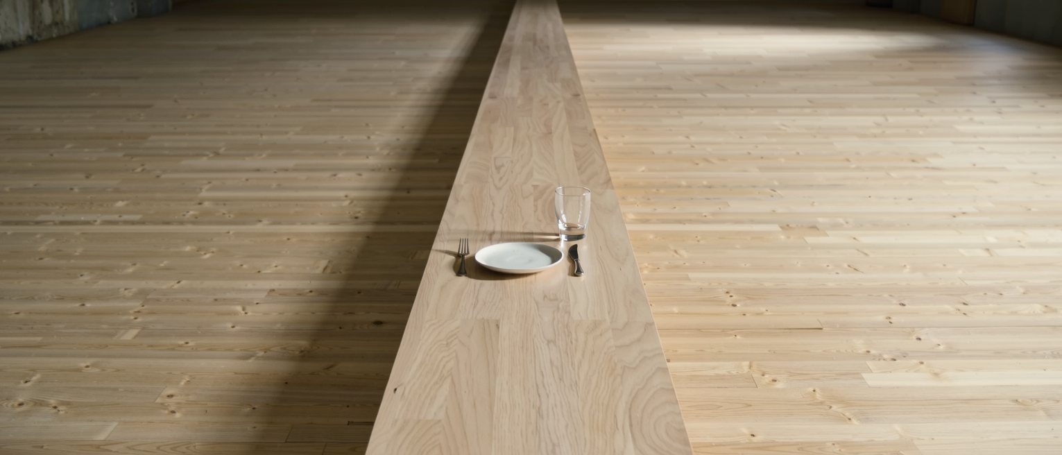 one single place setting alone at the end of a long bare table