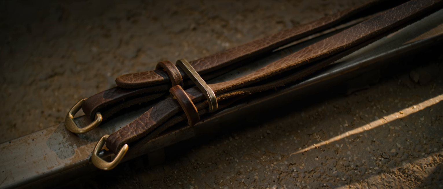 a pair of driving reins laid over a rail, the leather supple and the buckles down