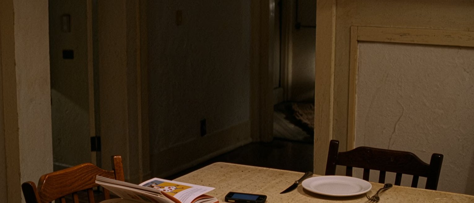 a phone lying face down on a kitchen table between a child's reading book and a single set place, the other chairs pushed in