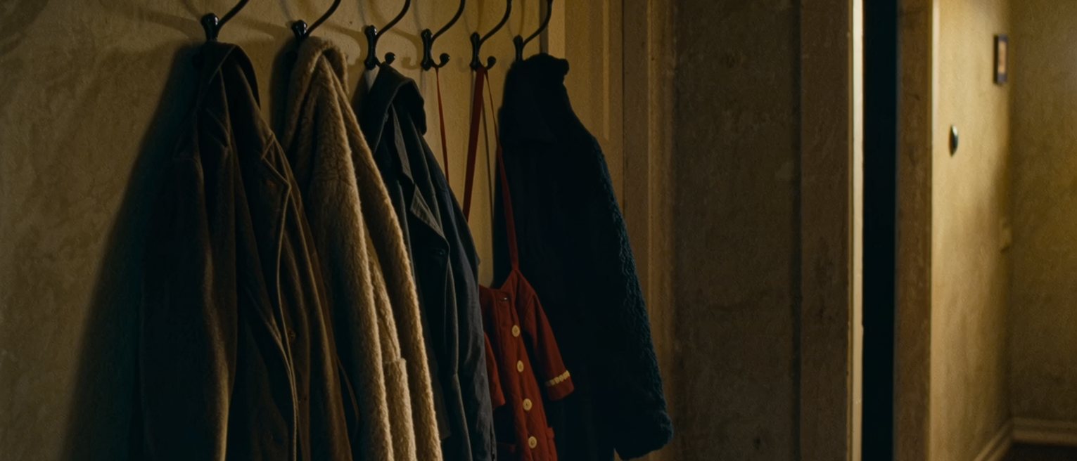 a hall with one adult coat and two small ones on the hooks, and a fourth hook standing empty