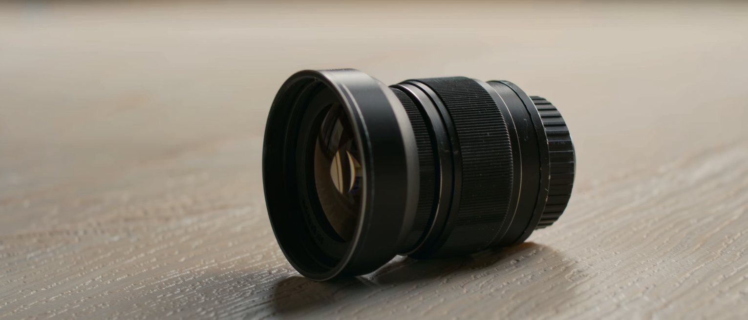 a ribbed black metal lens hood screwed onto a lens barrel, the front element dark