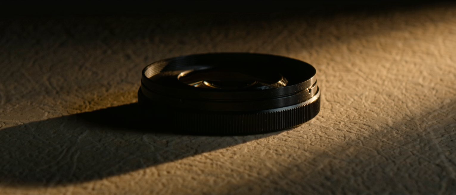 a ribbed black metal lens hood screwed onto a lens barrel, the front element dark