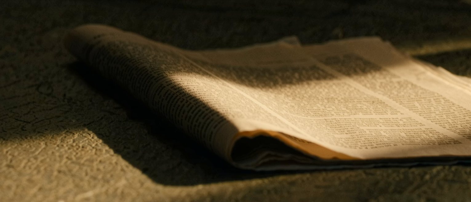 a folded newspaper gone soft at the crease, the column of type running off its edge