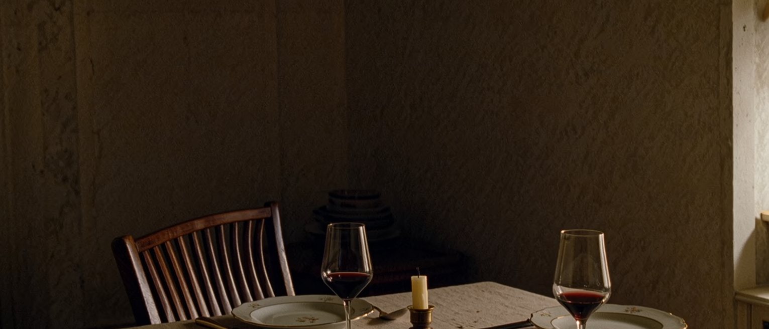 a dining table laid for two where one place has been set a clear hand's width further out from the table than the other