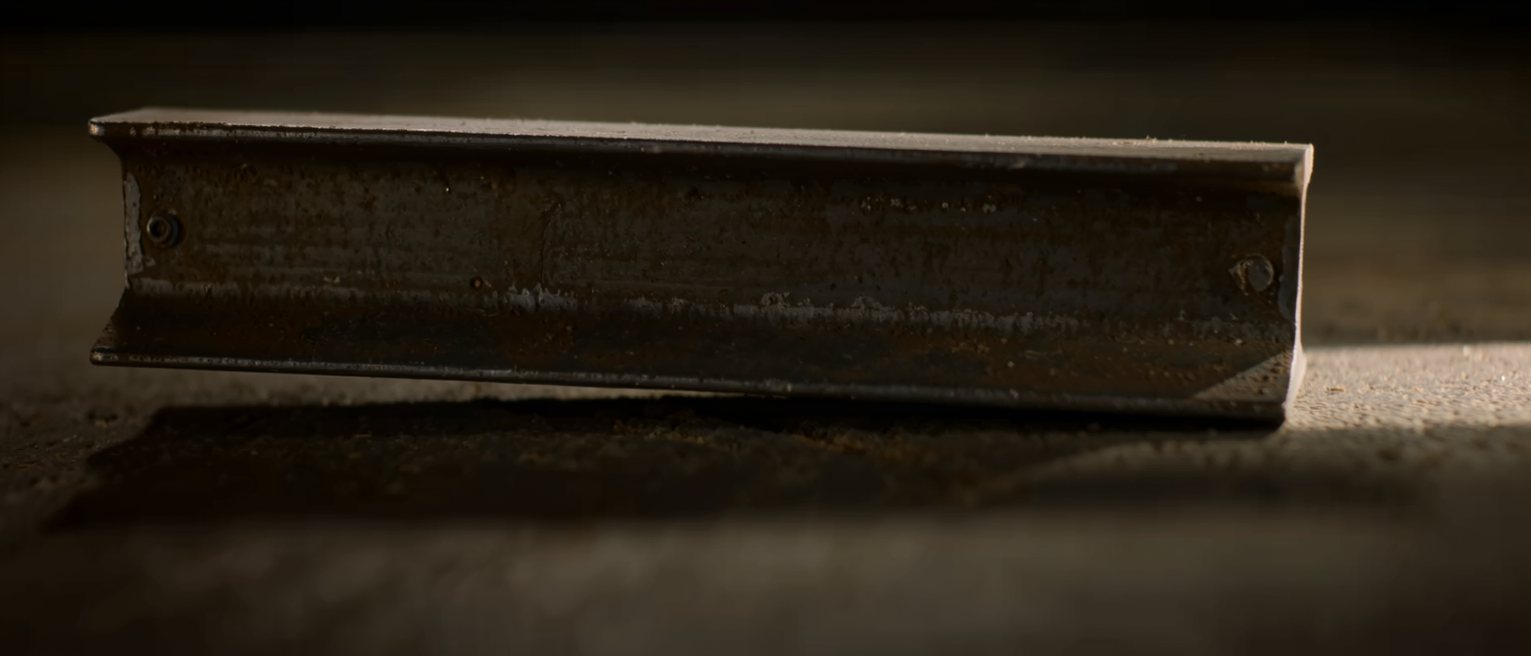 a thick heavy steel girder under load, its long span sagging visibly at the centre