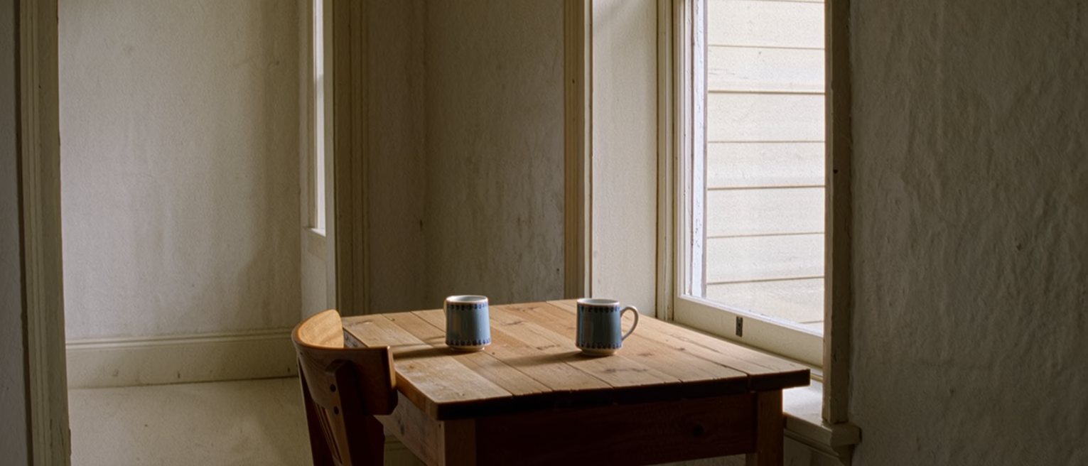 a kitchen table with two cups set down a few inches apart and not touching, the two chairs drawn in close on either side