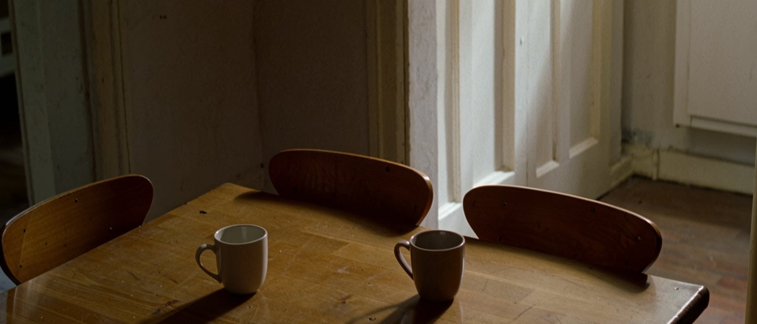 a kitchen table with two cups set down a few inches apart and not touching, the two chairs drawn in close on either side