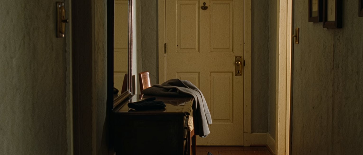 a hall seen close with a coat laid ready over the chair, one glove on the console and the other on the floor beneath it, the front door and its brass latch close behind
